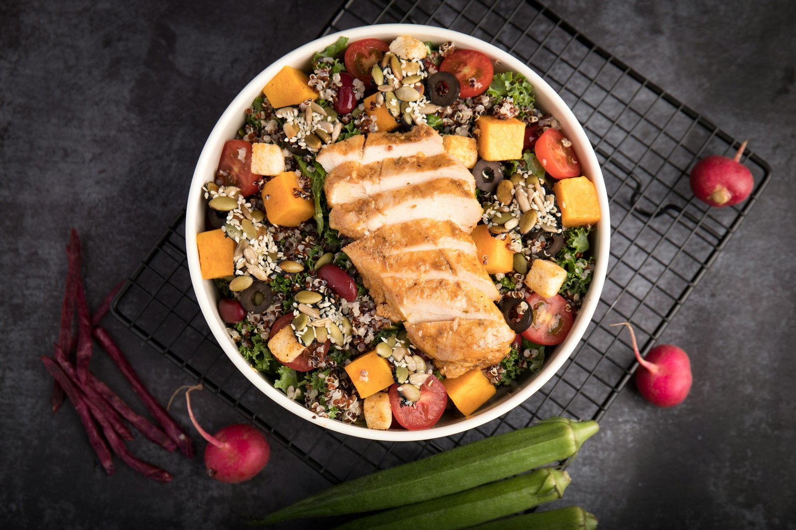 A vibrant bowl of grilled chicken salad with quinoa, fresh vegetables, and seeds.