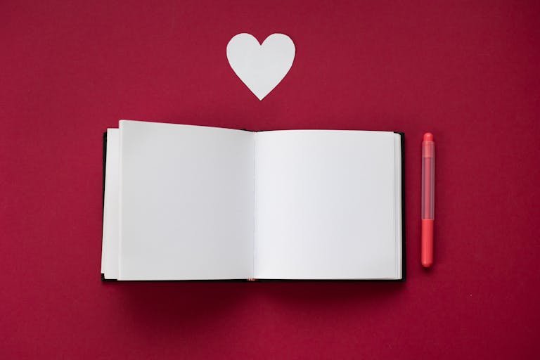 Top view of an open notebook with a heart cutout on a red background.
