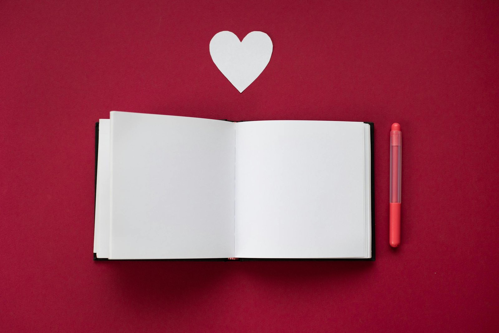 Top view of an open notebook with a heart cutout on a red background.