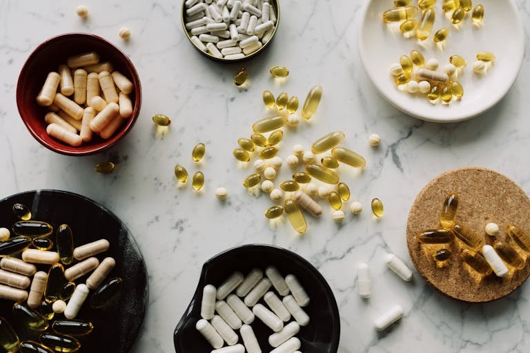 Variety of capsules and pills displayed in bowls on a marble table, ideal for healthcare concepts.